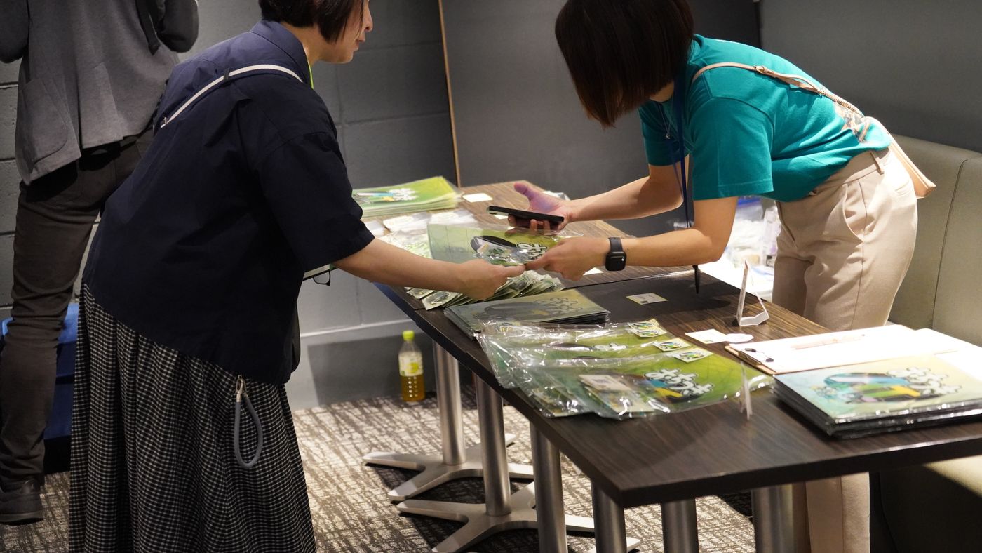 受付横のグッズ売り場で、参加者がグッズを手に取っている