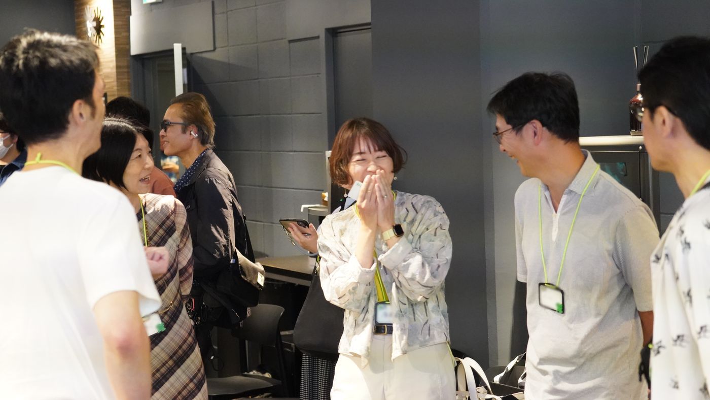 口元を手で押さえて笑う参加者と、まわりで話す人たち