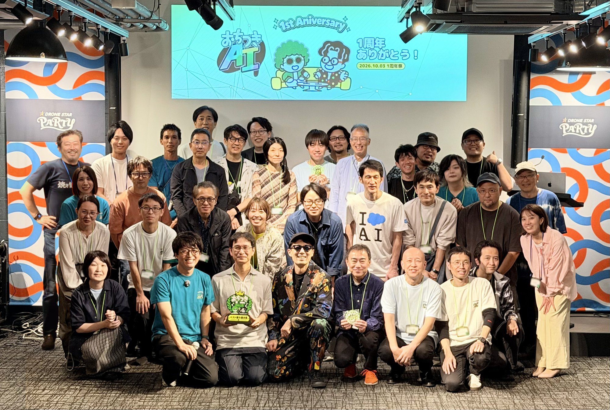 1周年祭の最後に撮った集合写真。スクリーンに「1周年ありがとう！」の文字